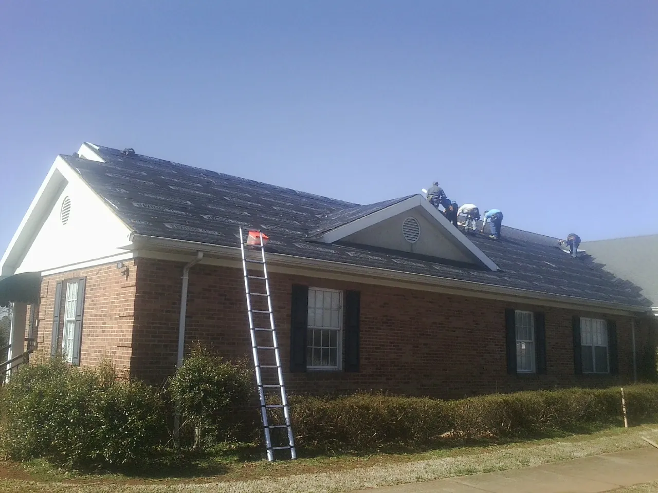 Crew tearing shingles off a brick ranch roof with a ladder set — Metal Roof Repair work by our crew in Agate