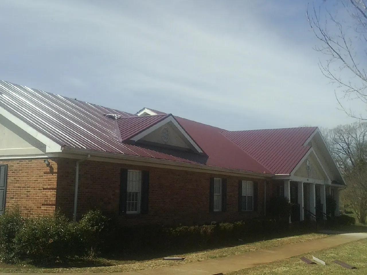 Red metal roof with gabled entries on a long brick building, from a Hail Damage Roof Repair job in Agate