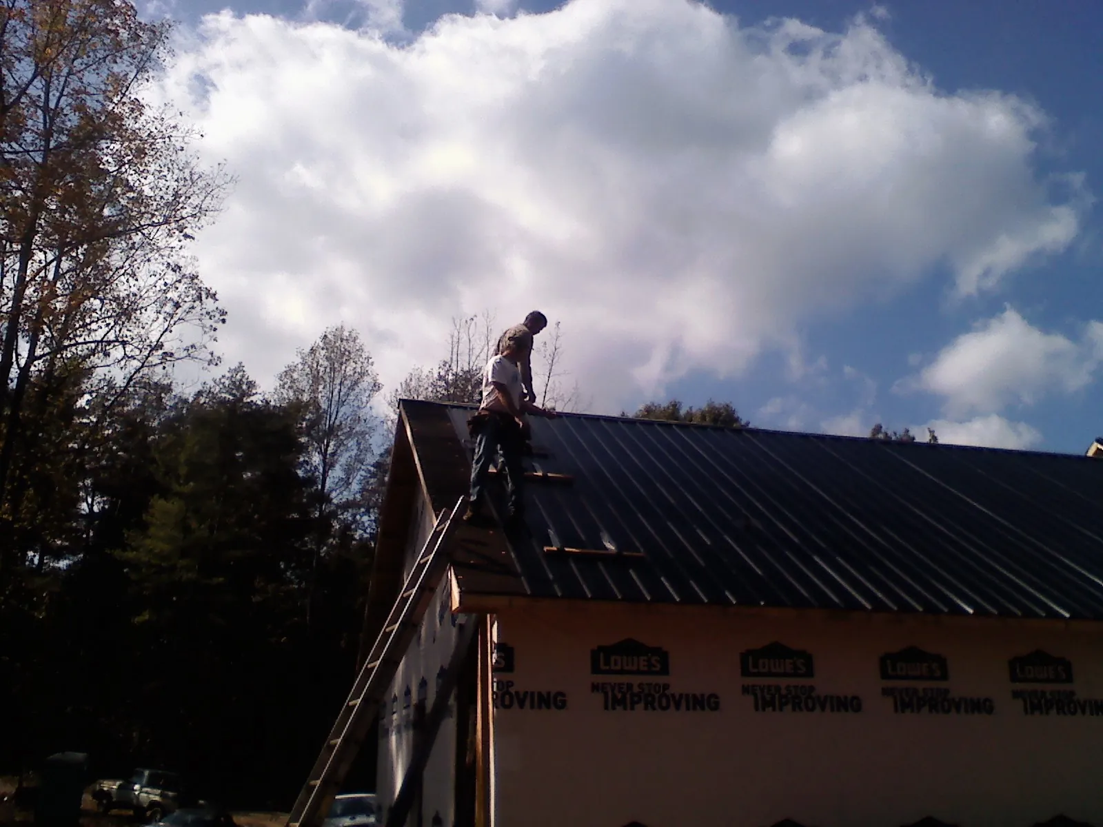 Roofer fastening dark metal panels high against a cloudy sky, from a Roof Inspection job in Agate
